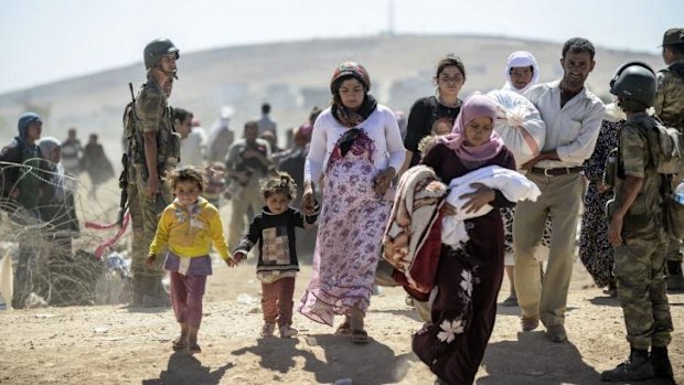 Syrian Kurds cross the border under the watch of Turkish forces.