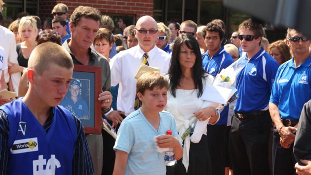 Jack Foy's father, Pat (holding picture), mother, Linda (with flowers), and brother, Matt (holding drink bottle) at the funeral.
