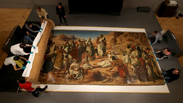 Conservators and volunteers carefully roll out a large-scale John Herbert painting at the National Gallery of Victoria.