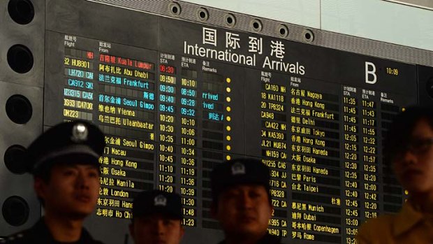 Chinese police in front of the arrival board showing Malaysia Airlines flight MH370 (top-red) at Beijing Airport.