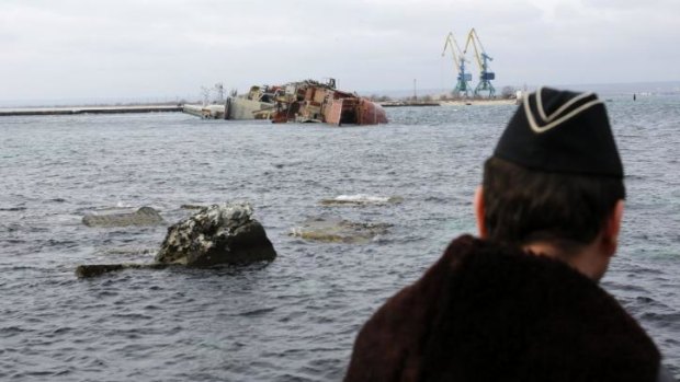 A Ukrainian navy sailor looks at the scuttled Russian ship from the Black Sea shore.