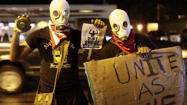 Masked demonstrators protest against the police shooting of 18-year-old Michael Brown by holding up signs on the streets of Ferguson, Missouri.
