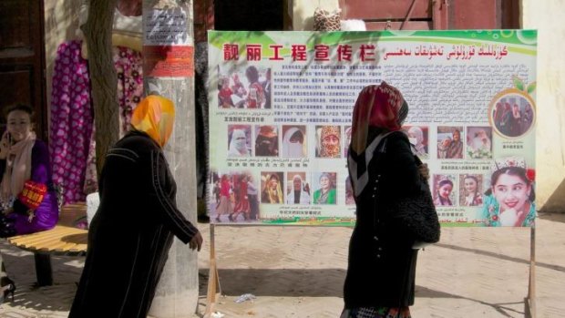Two women pass a billboard in Kashgar instructing Uighurs not to wear religious garments that cover their face.