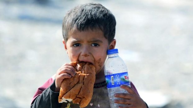 A displaced Iraqi boy from the Yazidi community eats a piece of bread and holds a bottle of water as he crosses into Syria at the Fishkhabur crossing, in northern Iraq.  