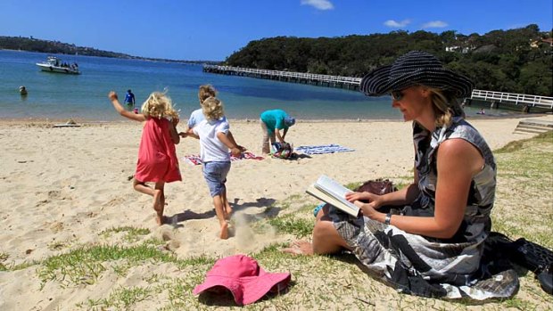 Still at the office ... businesswoman Cassandra Kelly, the joint chief executive of Pottinger, reads a book for work while her children enjoy Clifton Gardens beach in Mosman.