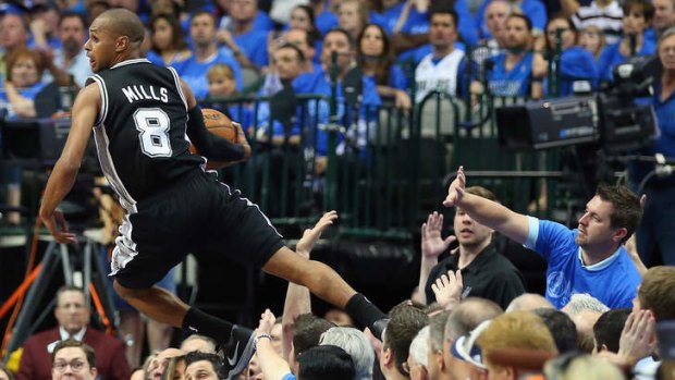 Spurs guard Patty Mills saves the ball from falling out of bounds as he jumps over fans against the Dallas Mavericks.