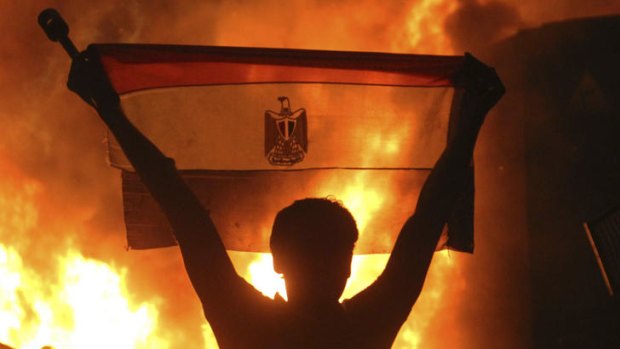 A protester holds an Egptian flag as fire rages outside the building housing the Israeli embassy in Cairo. Tensions between the countries has increased since the removal of Hosni Mubarak.