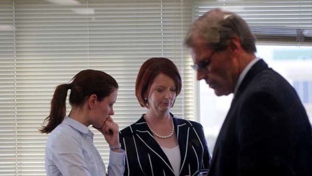 In the hands of fate ... Julia Gillard checks messages with her entourage including Senator John Faulkner and an assistant before facing the media at the Confoil factory in Seven Hills yesterday.