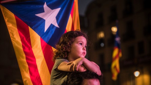 A child rests on a man's shoulders with "estelada" or pro independence flags in the background as pro-independence supporters gather in the square outside the Palau Generalitat in Barcelona.