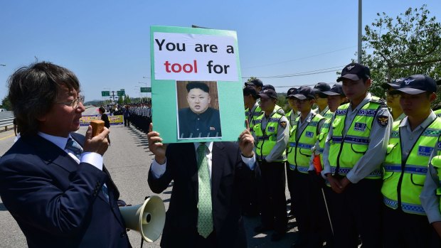 A South Korean conservative activist holds a placard showing a portrait of North Korea's leader Kim Jong-Un as policemen surround him during a protest against the border crossing by the women.