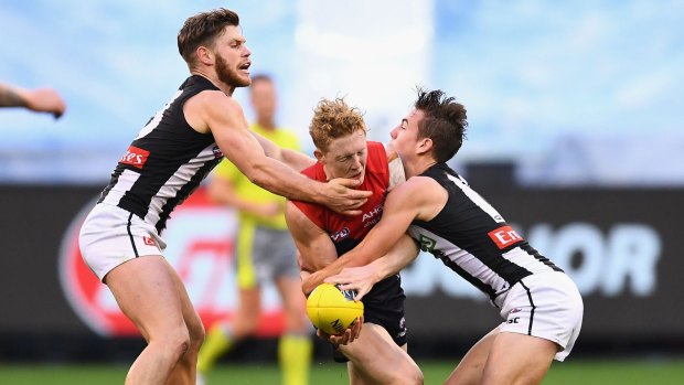 Clayton Oliver of the Demons is tackled by Taylor Adams and Callum Brown of the Magpies. 