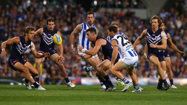 Ryan Crowley of the Dockers handballs as Brent Harvey of the Kangaroos approaches during the match between Fremantle and North Melbourne.
