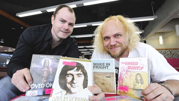 Mark Ryan and Andrew Leavold show off some of the rare cult titles that now feature as part of the research library at QUT Kelvin Grove.