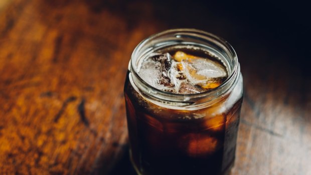 Jam jar filled with iced coffee: Cold Brew placed on a worn rustic wood surface. Strong contrasty light. Cold brew coffee.?