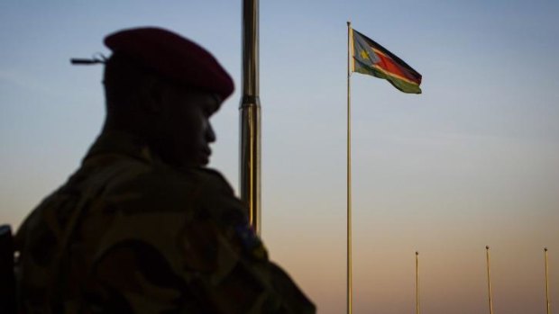 A South-Sudanese government soldier stands guard as a South Sudanese flag flies in the background in Juba, South Sudan.