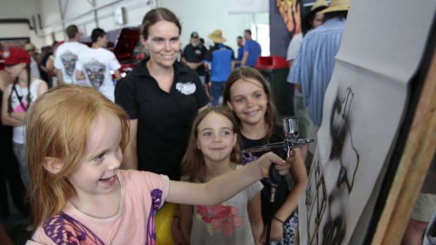 Helen Henry of Darwin, rear, watches as front from left, her daughters Olivia 4, Imogen, 7 and Natasha, 10 try out air brushing at the Anest Iwata stand.