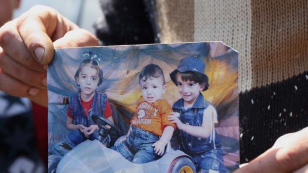 Burnt to death ... a mourner holds a picture of the three Bashir children, Nadine, Sabre and Farah (from left), who died in a fire in their home.