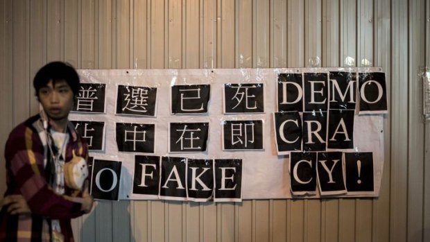 A protester stands next to a banner that reads "No Fake Democracy!" outside government offices in Hong Kong on Friday.