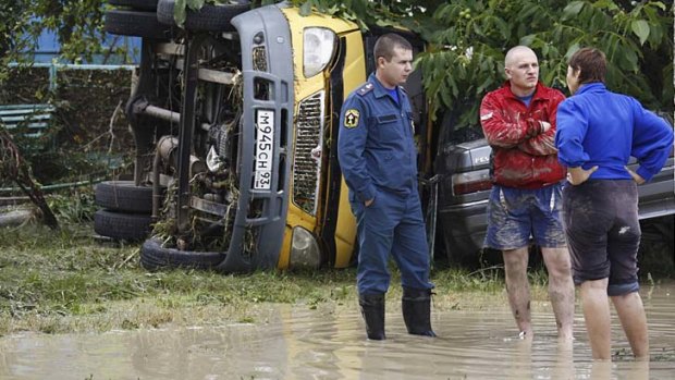 An emergency service worker, left, stands near an overturned car in the southern Russian town of Krymsk.