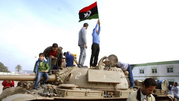 Libyans stand on a tank holding a pre-Gadhafi era national flag inside an army compound in Benghazi.