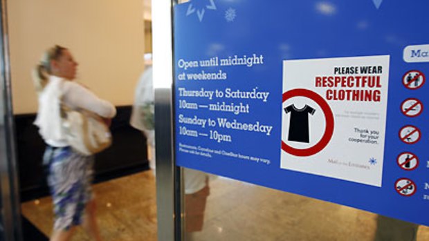 A Western woman walks in a shopping mall as she passes by a dress code sign at a shopping mall in Dubai.