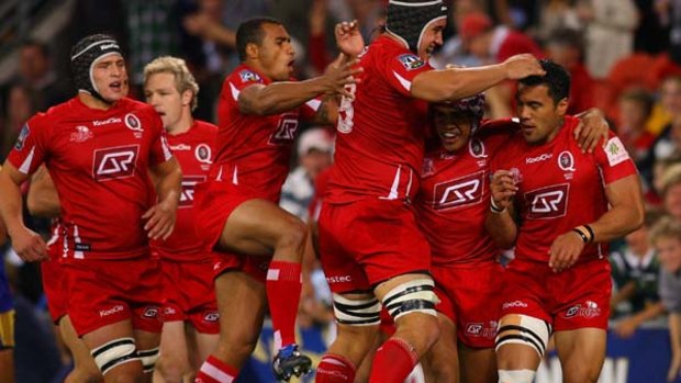 Digby Ioane of the Reds celebrates with teammates after scoring a try against the Highlanders.