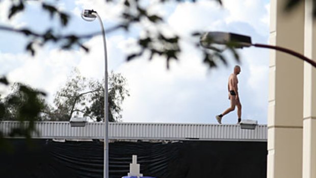 A naked man thought to be carrying a handgun was surrounded by police on Saturday after he climbed atop a Perth city billboard.