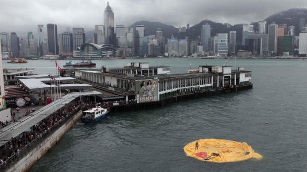 A workman (R) stands on the remains of a 16.5-metre-tall inflatable rubber duck art installation as it lies deflated in Hong Kong's Victoria Harbour.
