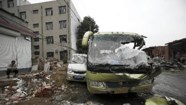 A man smokes near smashed vehicles at Yuanshi county, in north China s Hebei province. A drunken shovel loader driver went on a rampage in northern China, smashing into shops and vehicles and killing 11 people. Photo: AP