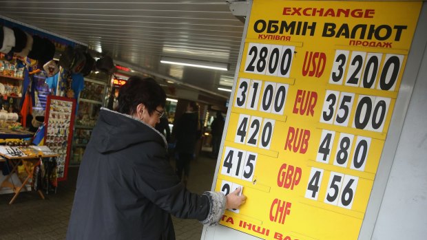 A woman prepares a board showing the day's exchange rates of the Ukrainian hryvnia against major currencies at a kiosk in Kiev on February 21. The Ukrainian hryvnia has lost over half of its value since the crisis in Crimea last year.