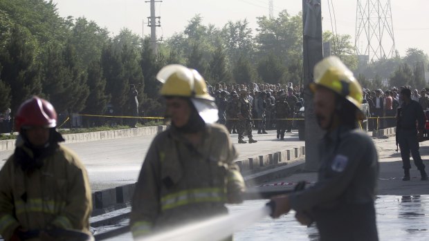 Afghan firefighters clean a street as people watch at the site of a suicide attack that killed at least 14 people in Kabul, Afghanistan, on Monday.