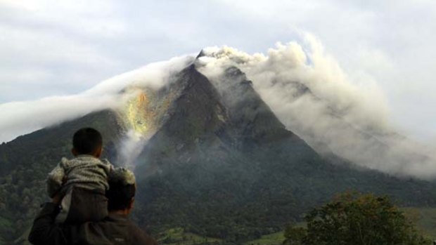 Exodus . . . a father and son look on as Mount Sinabung burns, spreading ash up to 30 kilometres away.