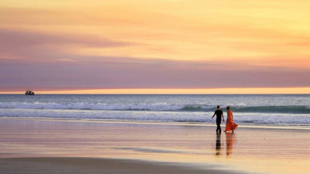A young couple walking on Cable Beach, Broome, Western Australia, at sunset.