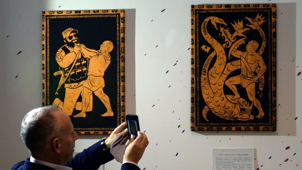 A visitor takes photos during the '12 Labors of Putin' art exhibition on Monday, 2014 marking the 62nd birthday of Russia's President Vladimir Putin at the design workshop in Moscow.