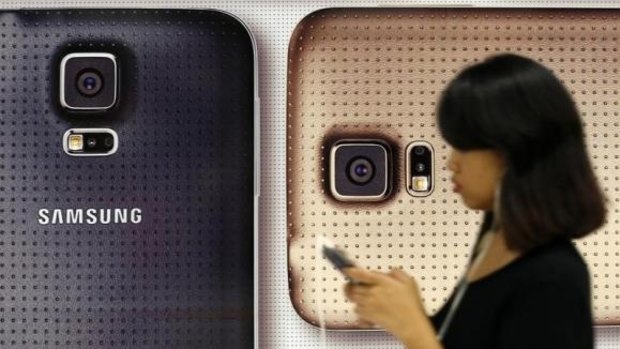 A commuter uses her mobile phone as she walks past a Samsung Galaxy mobile phone advertisement.