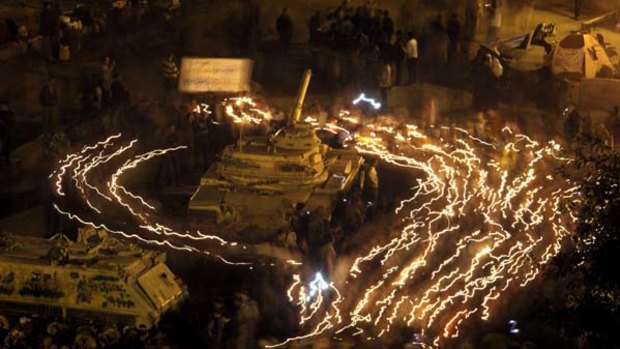 Cursing the darkness ... demonstrators  hold candles in remembrance of the uprising's victims as they circle an army tank in Cairo's Tahrir Square on Wednesday.