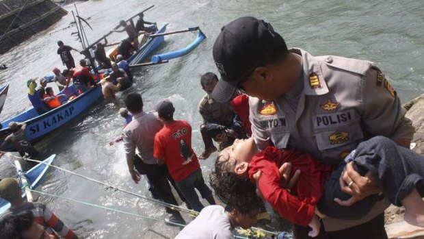 A police officer carries an unconscious child who was on a boat that capsized.
