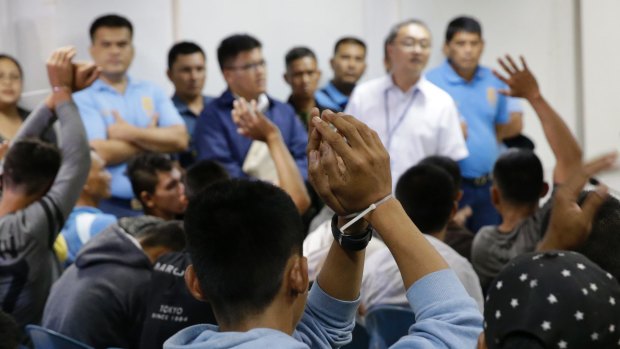 Men suspected to be Islamist militants raise their zip-tied hands, as they arrive at the Department of Justice in Manila>