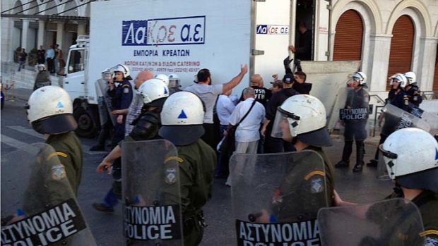 Members of the Golden Dawn party try to organize the unloading of food from a truck as riot police look on in central Athens.