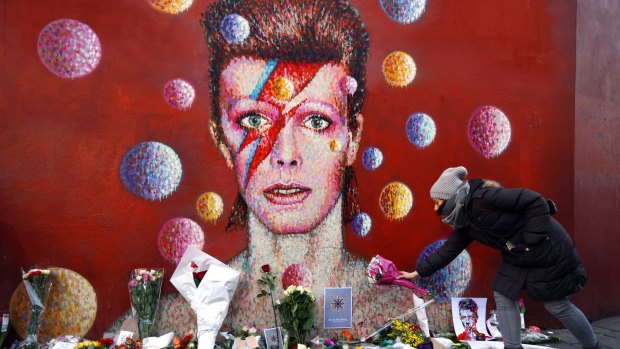 A woman leaves flowers beneath a mural of David Bowie in Brixton.