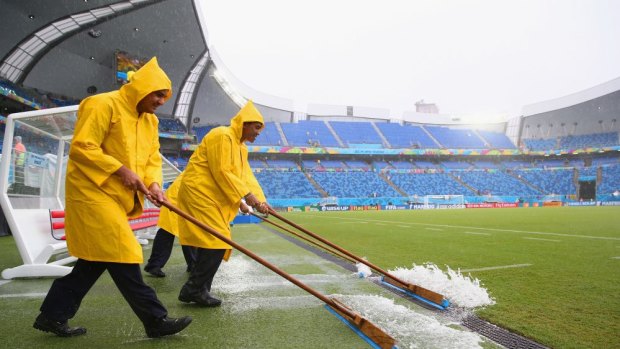 Stadium workers sweep rain water off the field toward a drain before the between Mexico and Cameroon at Estadio das Dunas in Natal, Brazil. 