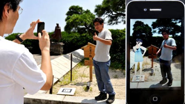 A man stands next to a tiny black and white panel to have his picture taken and displayed including the animated image of a girl through an iPhone application at the famous spot of Kanichi and Omiya in Atami, southwest of Tokyo.