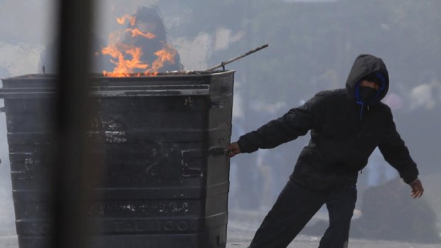 A masked youth pulls a burning garbage bin set on fire by rioters in Hackney.