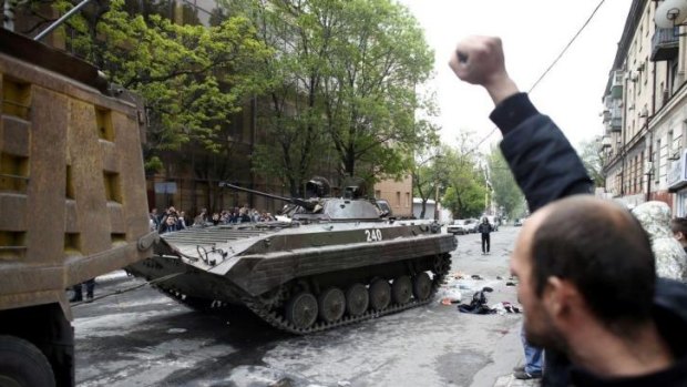 A man celebrates as a broken tank  left behind by Ukrainian forces is taken away by  pro-Russian militants in Mariupol after the clash.