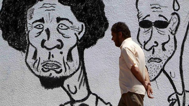 A man walks past caricatures of Libyan leader Muammar Gaddafi (left) and his son Saif near a courthouse in Benghazi1.