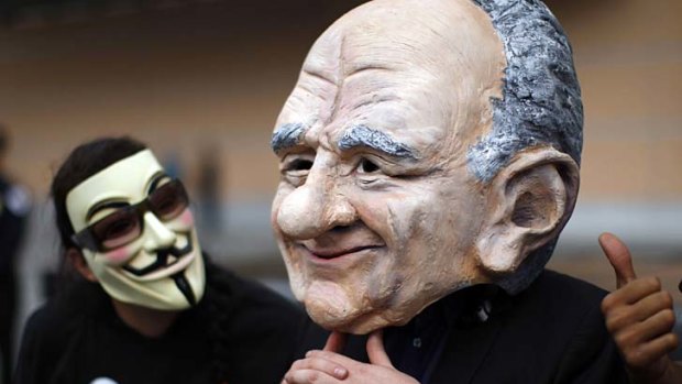 A demonstrator wearing a mask looks at a puppet head representation of Rupert Murdoch, as protesters demonstrate at Fox Studios during the annual News Corp shareholder meeting in Los Angeles.