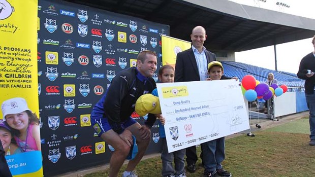 Freshly shaven Bulldogs Coach Des Hasler presented a $100,000 cheque to Camp Quality earlier this year.