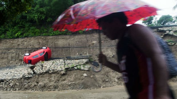 A passer-by walks near a car that fell after part of a hill collapsed in Acapulco, Guerrero state, Mexico during the passage of Tropical Storm Manuel.