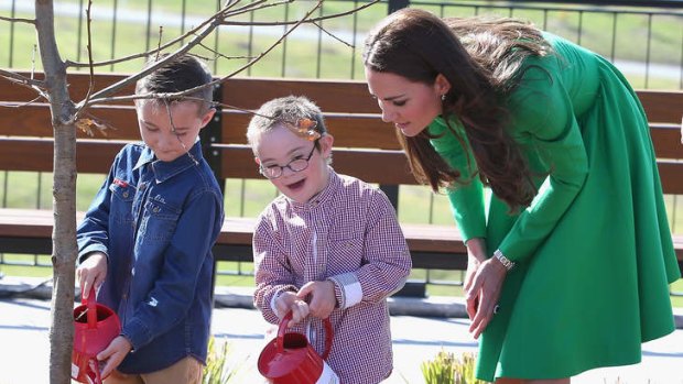 Catherine, Duchess of Cambridge watches two children help her with a tree planting.