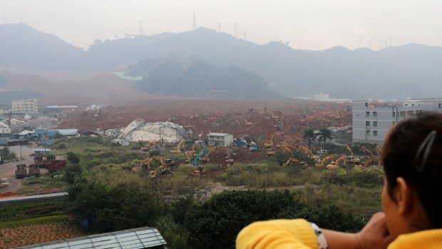 A woman watches rescuers  search for survivors near collapsed buildings following the landslide in Shenzhen.